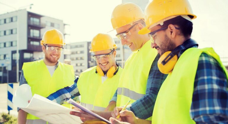 A team of contractors reviewing blueprints at a construction site.