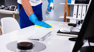 A cleaner sanitizing office desks with professional-grade supplies in a modern office environment.